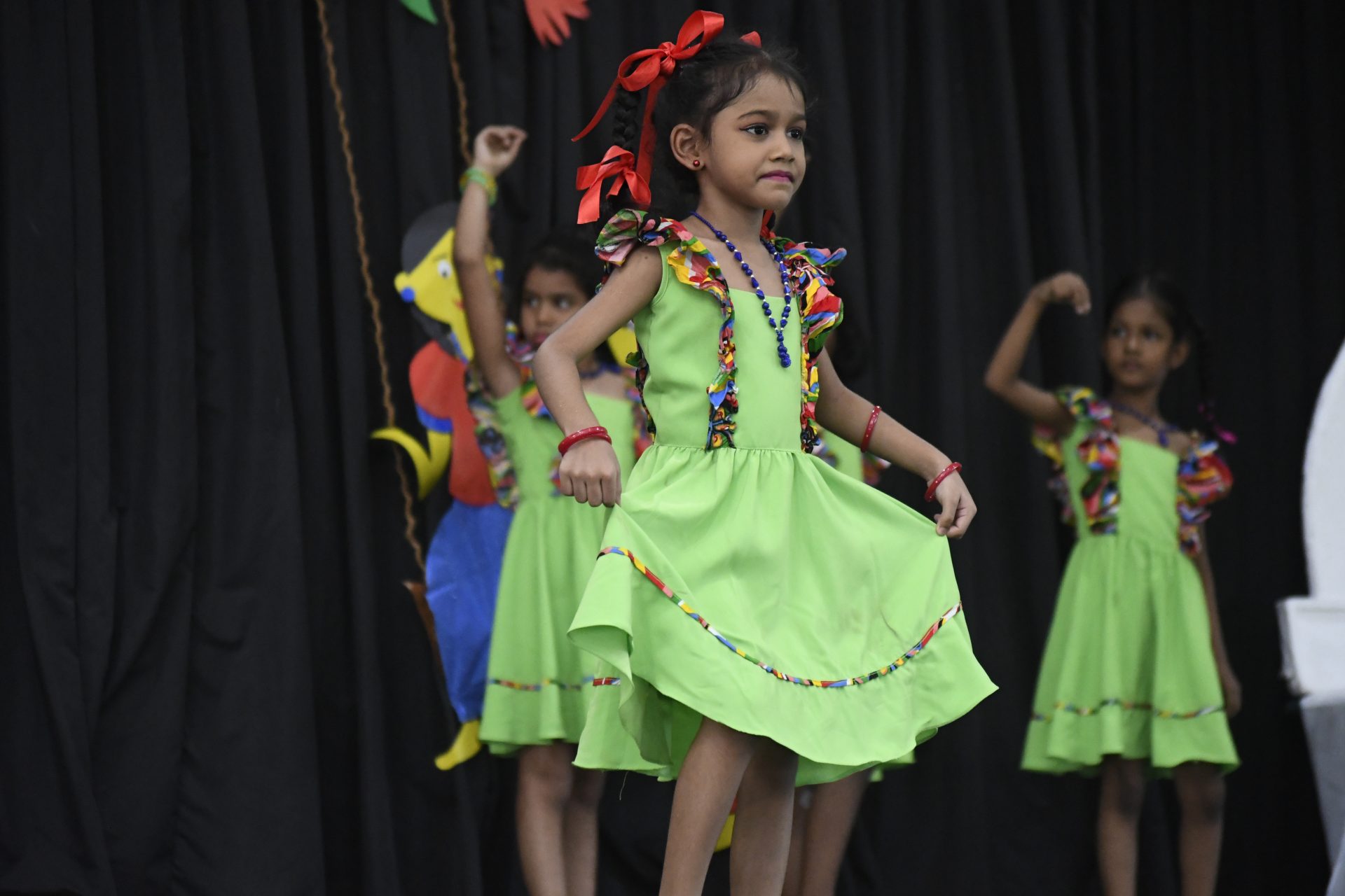 Young girls dancing in colorful lime green dresses on stage.
