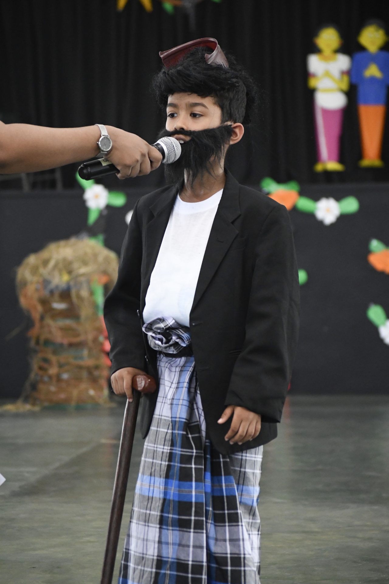 Child in traditional costume with cane, speaking at cultural event.