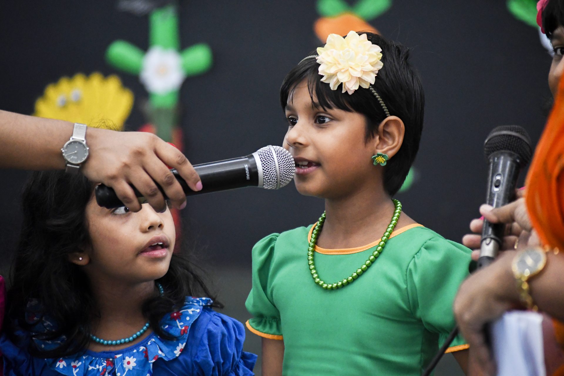 Two girls speaking at a festive event with colorful decorations.