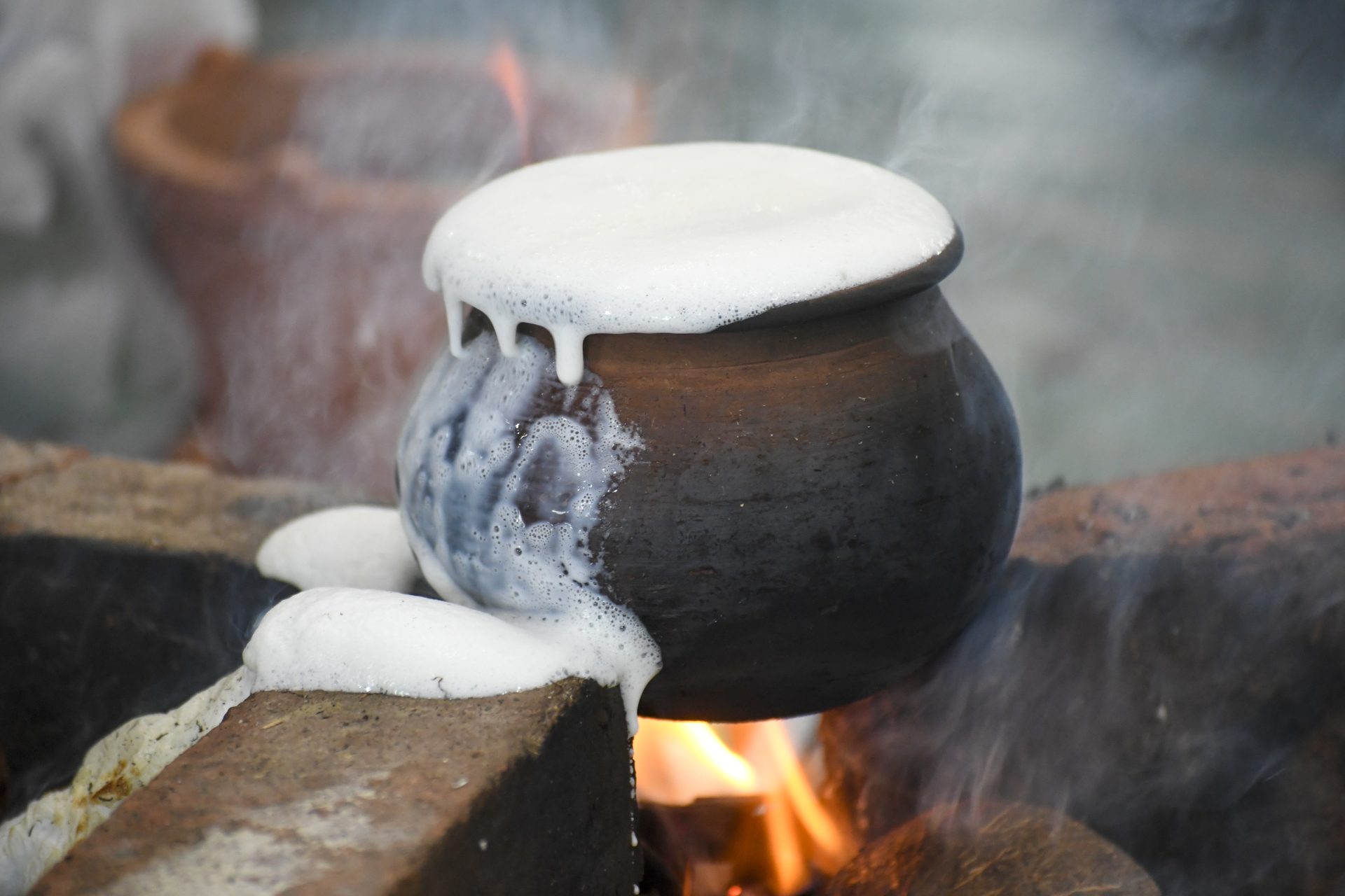 Boiling milk over a rustic open flame in a darkened clay pot.