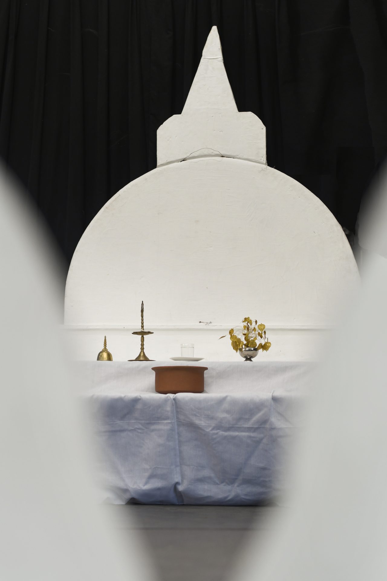 Ceremonial table with candle, wooden box, and yellow flowers in front of temple-like backdrop.