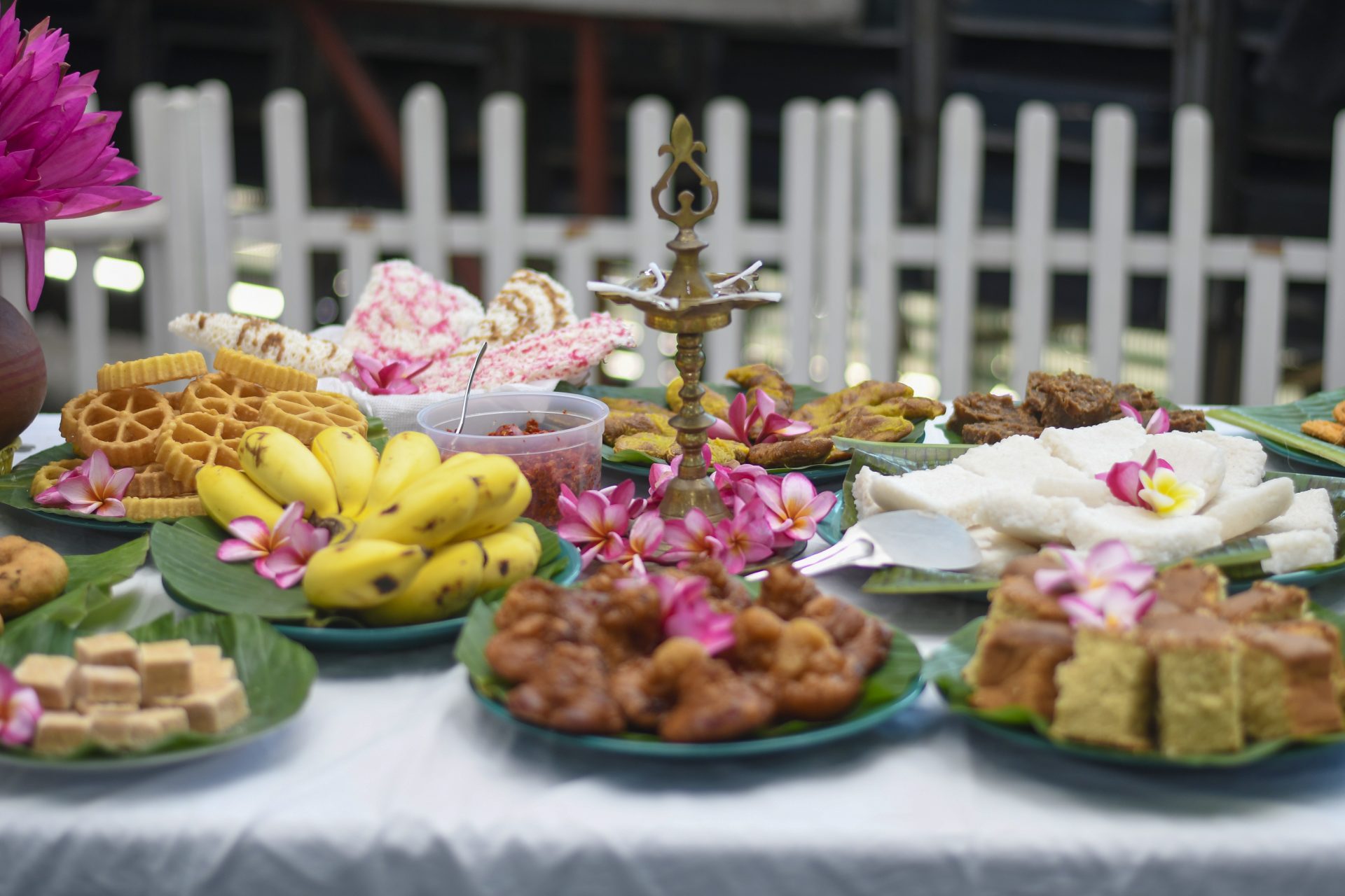 Festive table with traditional snacks, sweets, brass lamp, and flowers.