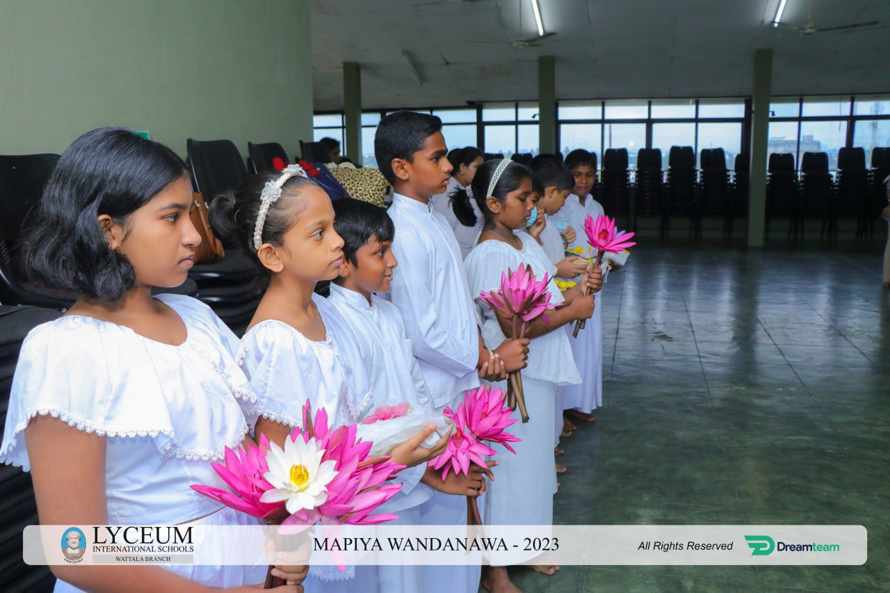 Children in white holding lotus flowers during Lyceum 2023 ceremony in a large hall.