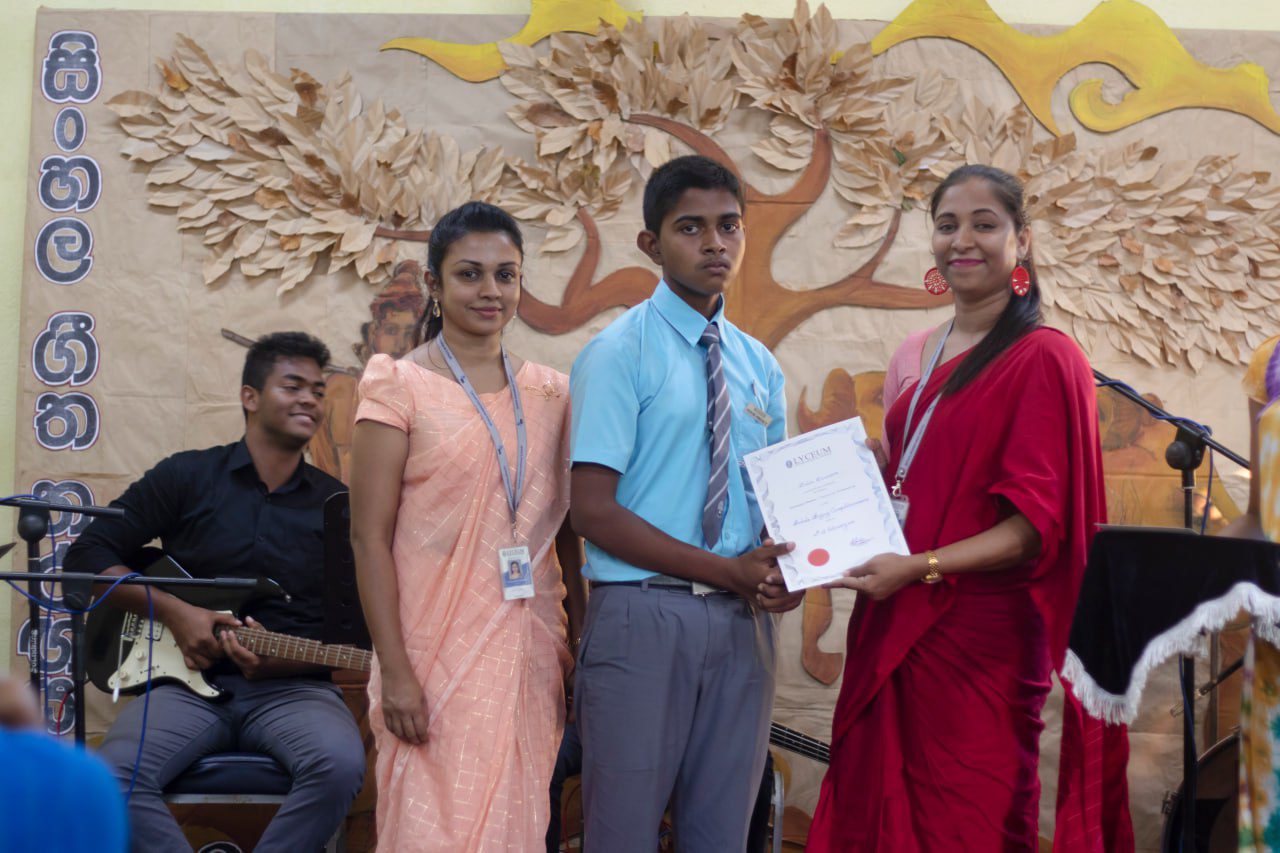 Young man receives certificate at academic event, surrounded by colorful attire and artistic backdrop.