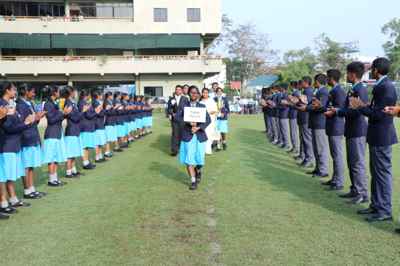 Students in uniform applaud during a school award ceremony on a grassy field.
