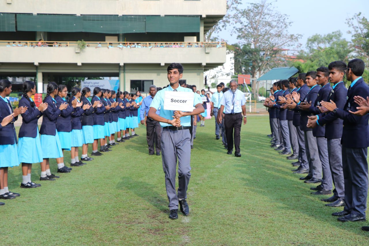 School ceremony with students clapping for a leader holding a Service sign.