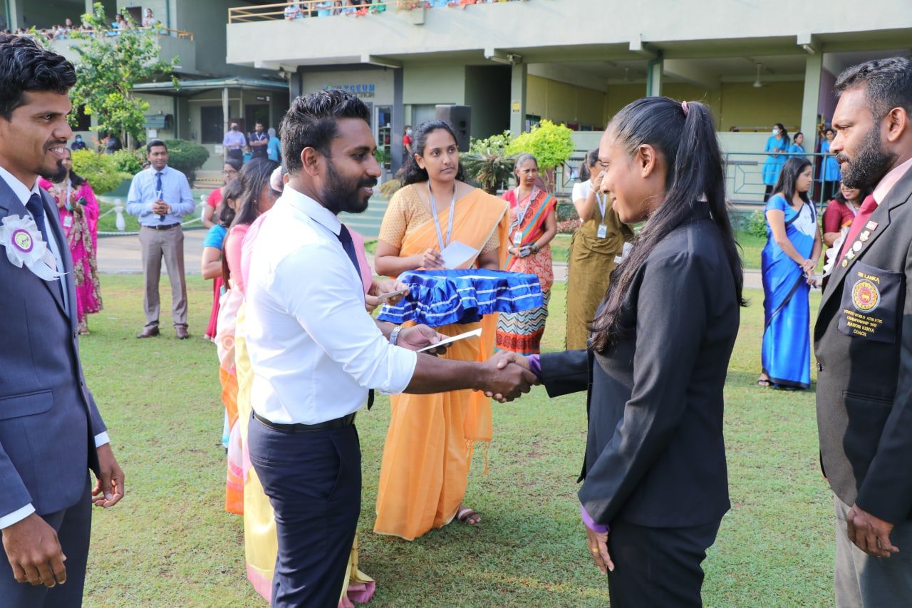 Formal ceremony with handshake and colorful attendees on a well-kept lawn.