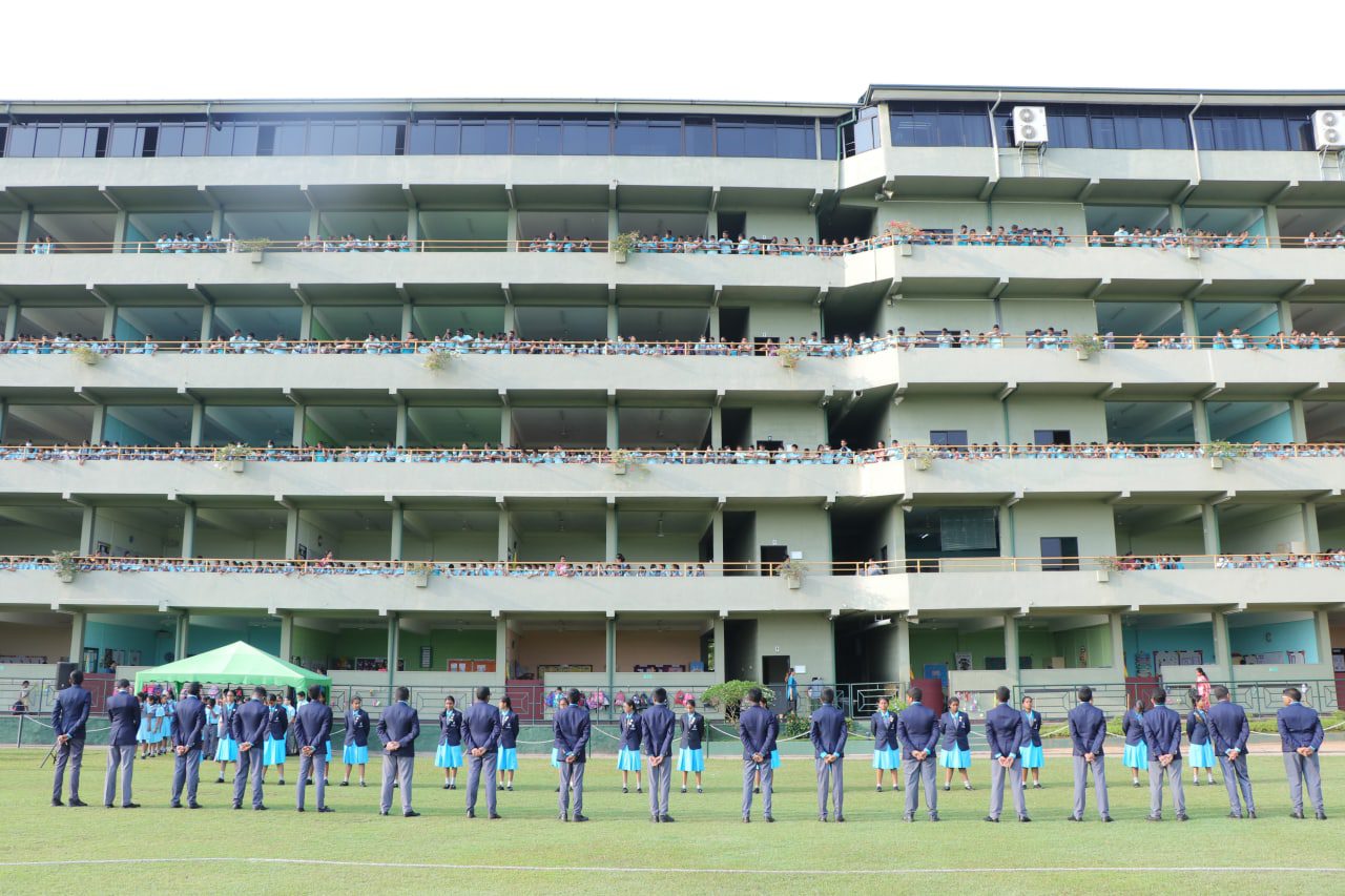 Uniformed students in formation on a lawn in front of a modern school building.