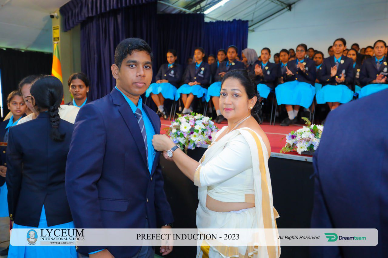 A teacher pins a badge on a student at Lyceum Prefect Induction 2023.