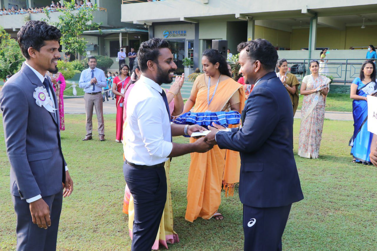 Outdoor ceremony with men in suits and women in sarees holding trays.