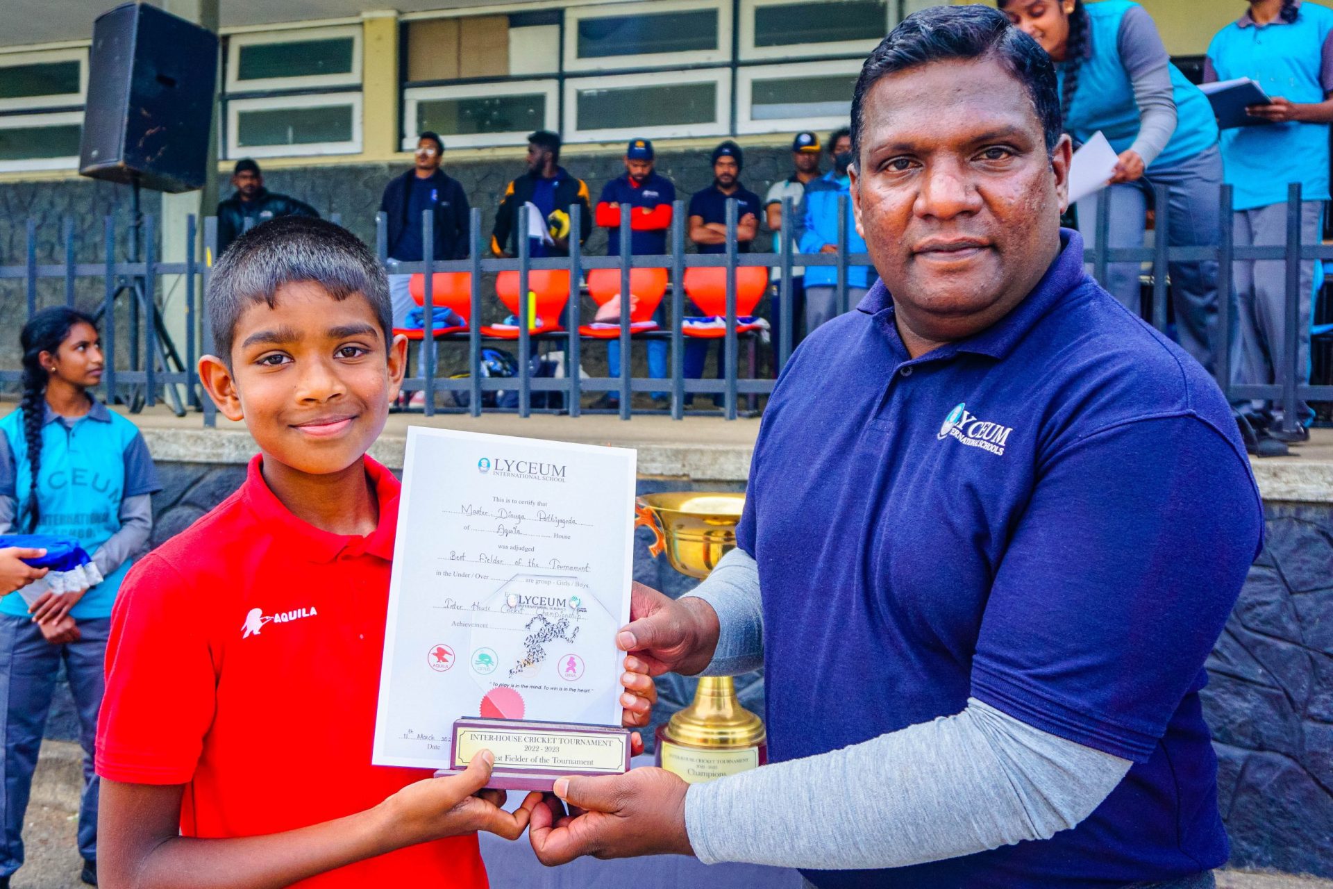 Young boy receives award from man at outdoor ceremony.