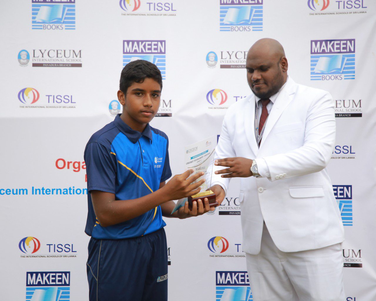 Boy receiving a trophy at an award ceremony with sponsor logos in the background.