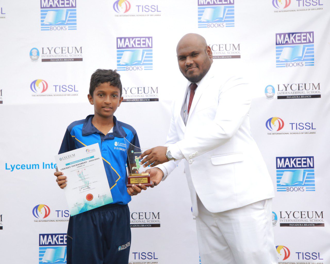 Young boy receives trophy from man in white suit at award ceremony.