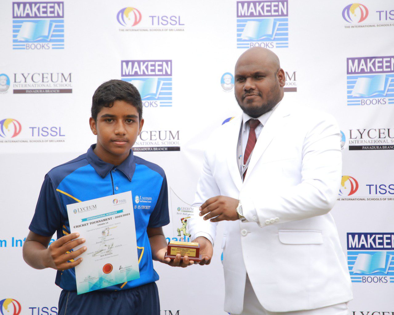 Young athlete receiving award from official at formal event with sponsor logos in the background.