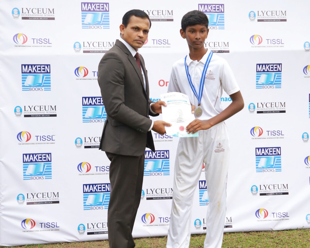 Young athlete receives a certificate from a suited man at a sponsored outdoor event.