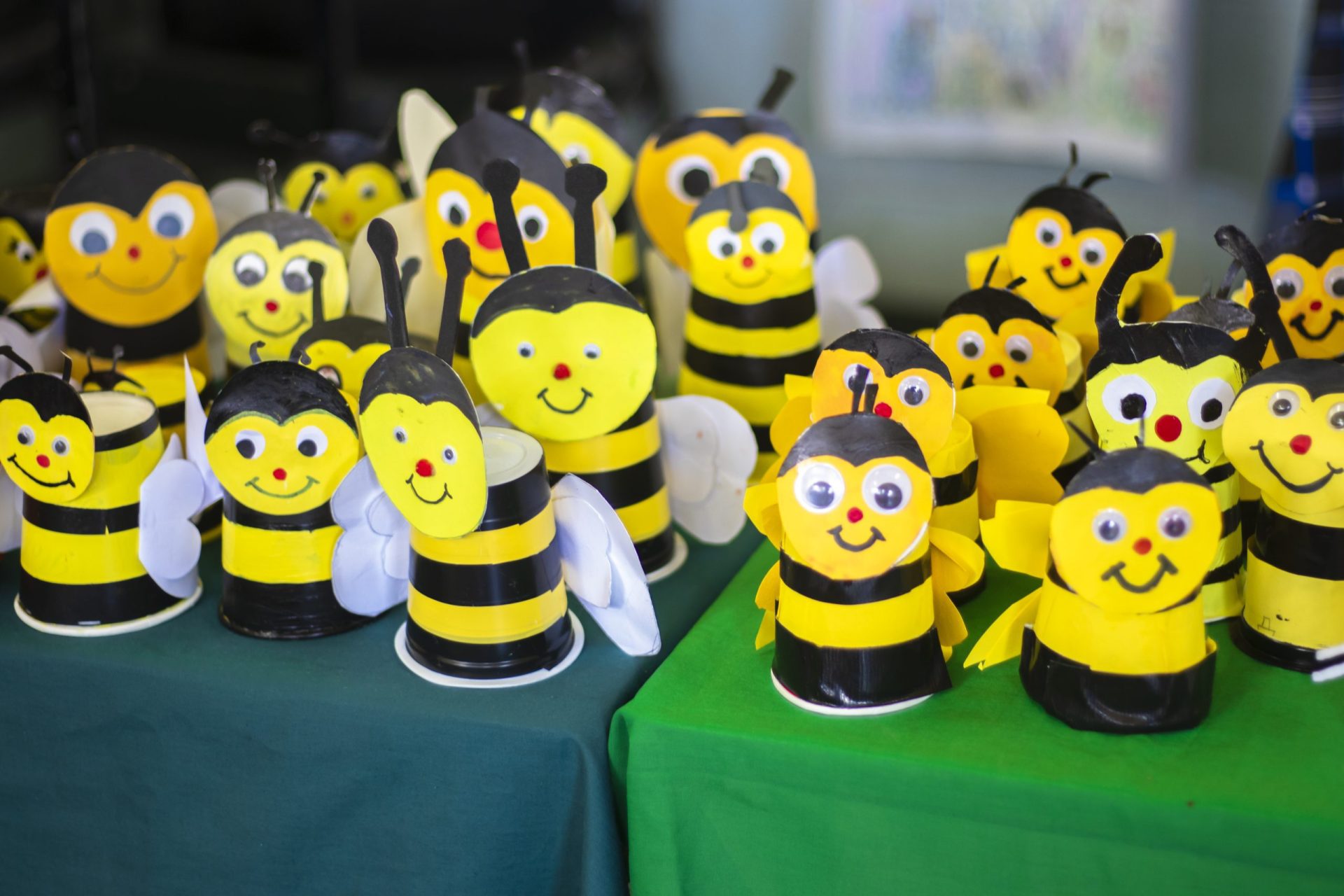 Handmade bumblebee crafts with colorful details on green cloth-covered tables.