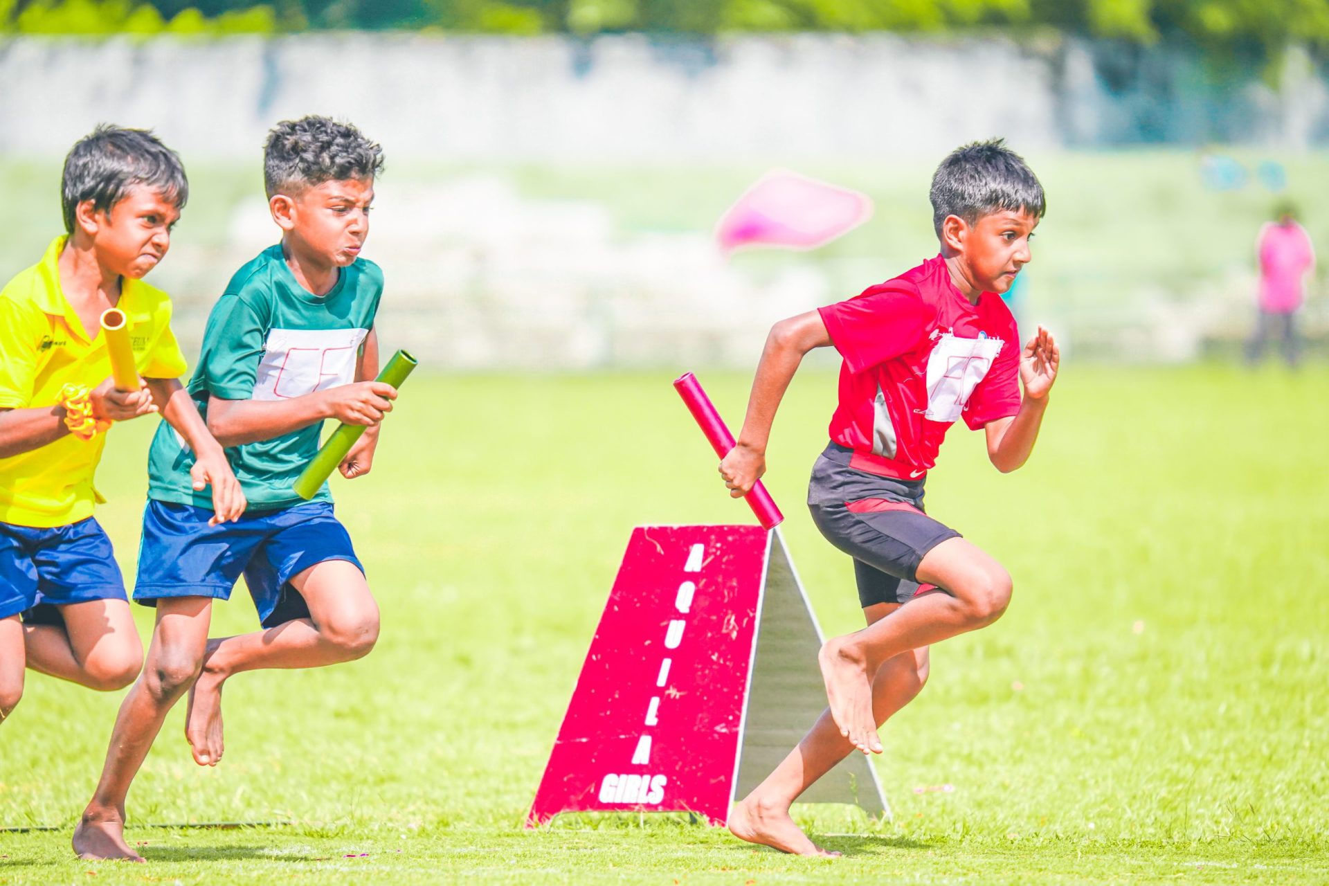Barefoot boys in colorful relay race on grassy field.