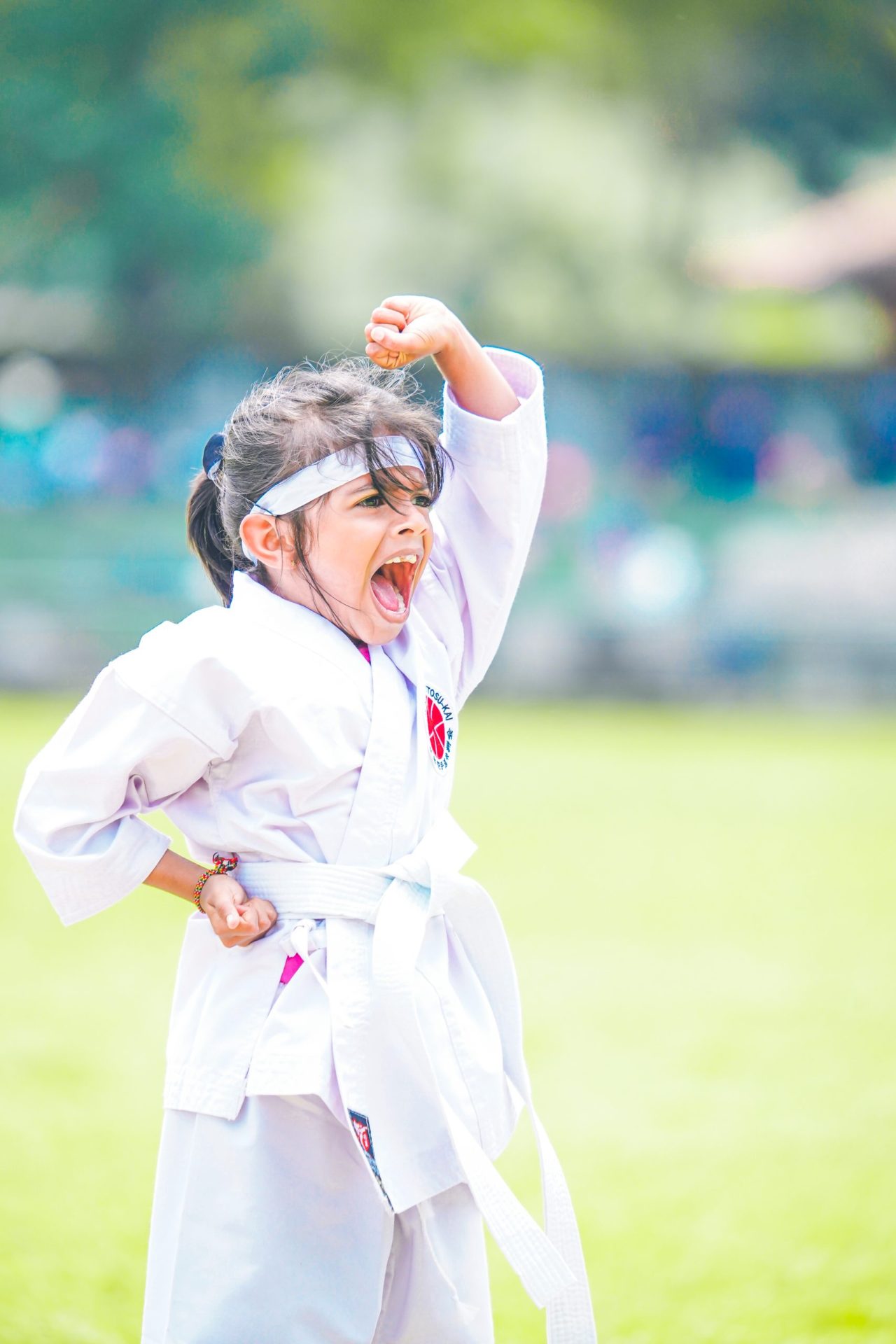 Young girl in white karate gi performing a dynamic move outdoors.