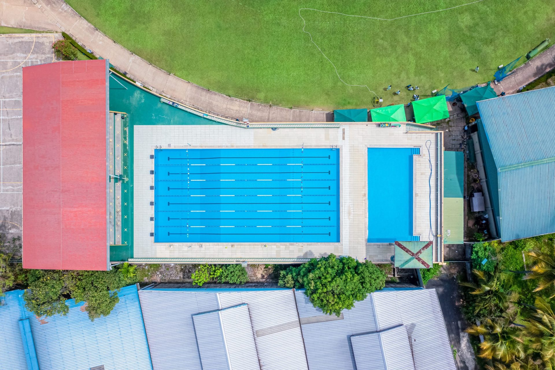 Aerial view of modern swimming pool complex with multiple buildings and surrounding greenery.