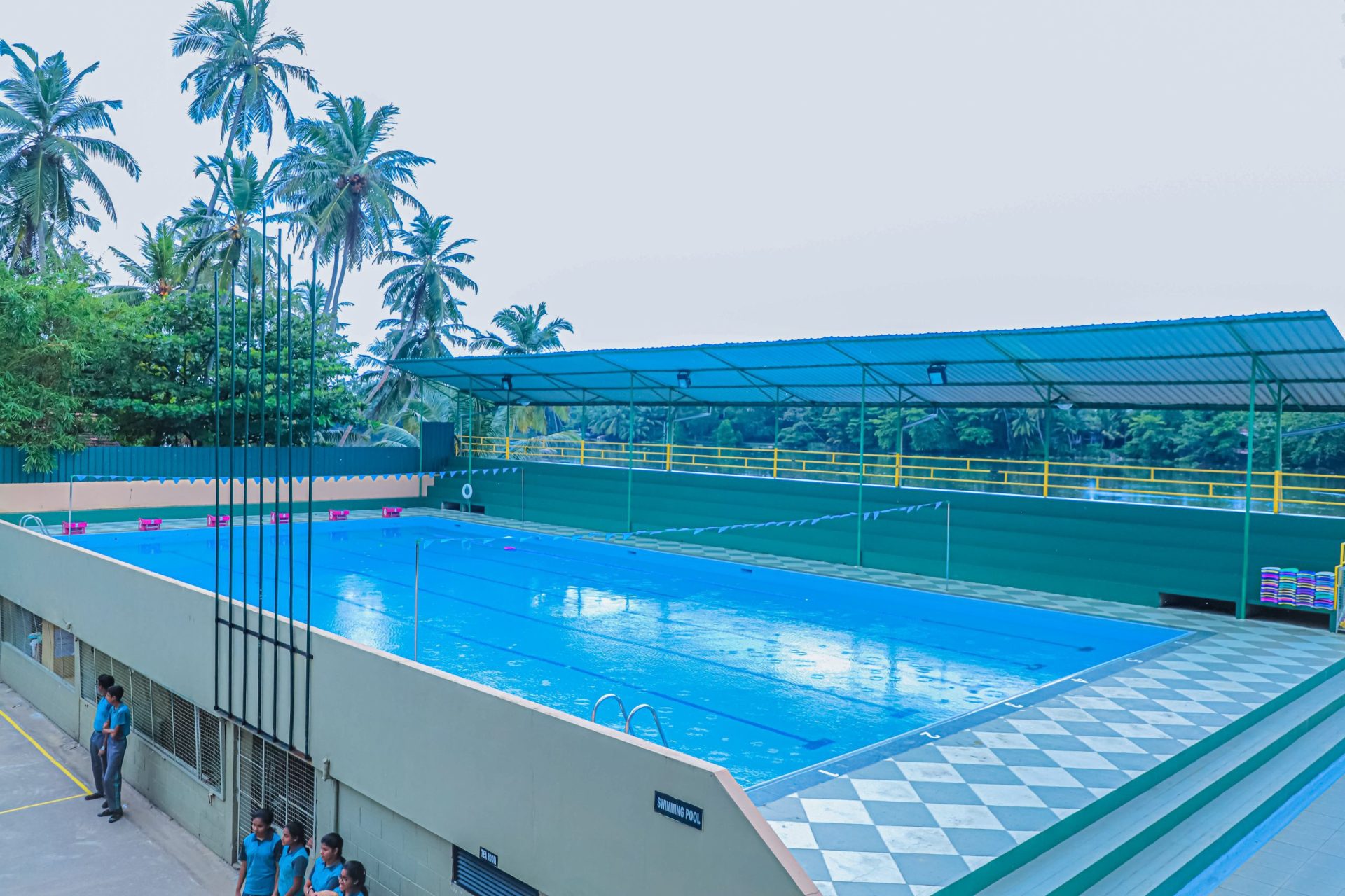 Rectangular tropical pool with lane markers, canopy, and lifeguards surrounded by lush greenery.