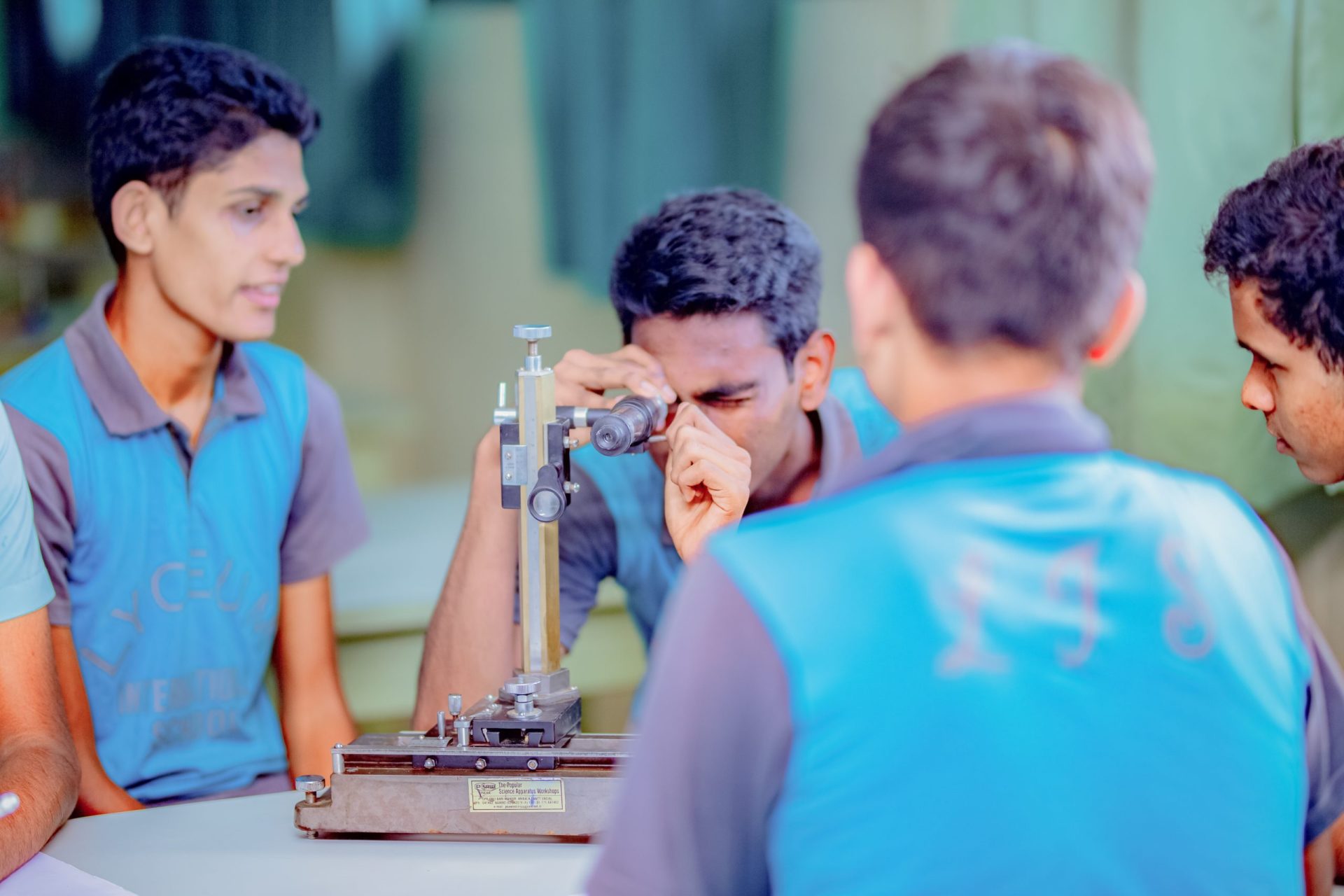 Students in blue uniforms conducting a science experiment with a microscope.