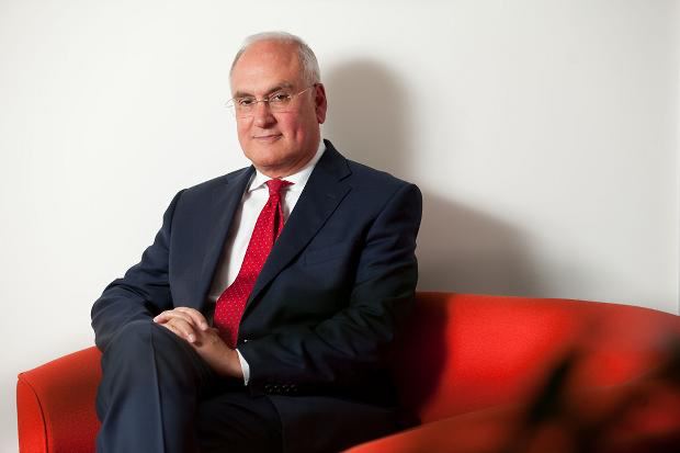 Sir Michael Wilshaw in Navy Suit on Vibrant Red Chair Sir Michael Wilshaw in navy suit on red chair, exuding confidence and professionalism.