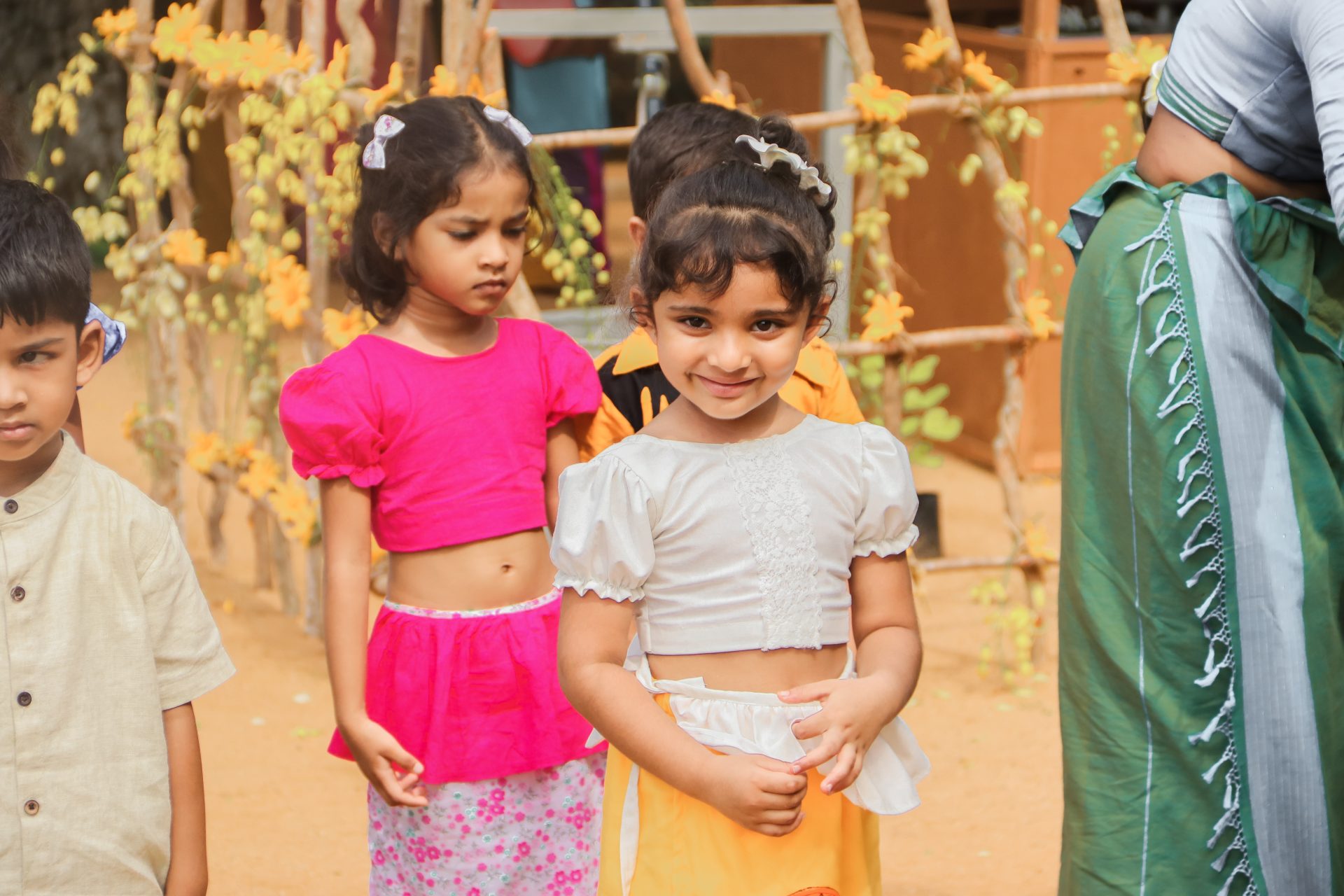 Children in vibrant traditional attire celebrating outdoors with flowers in the background.