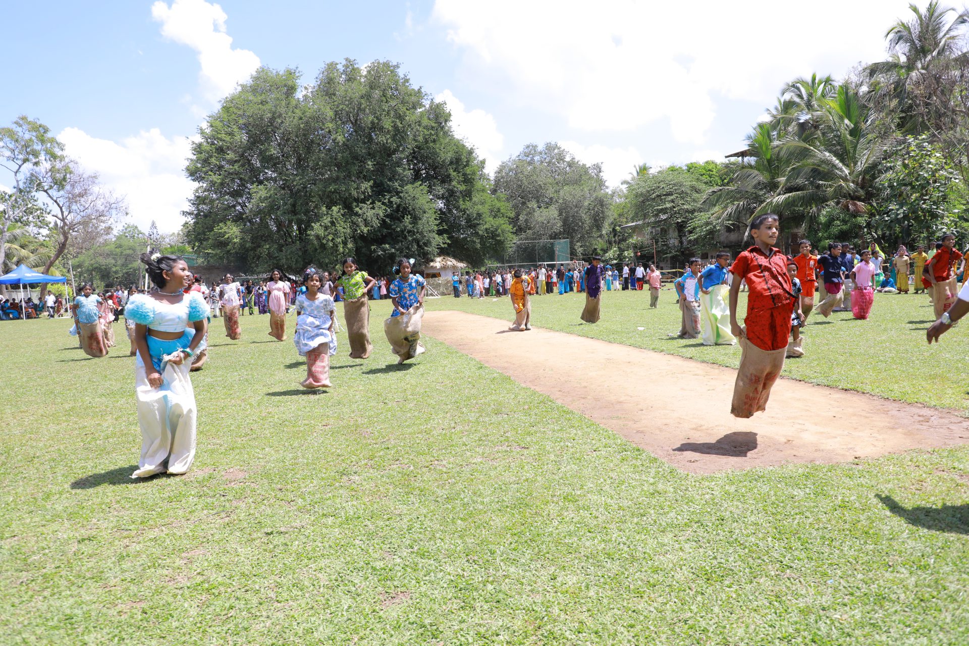 Participants in colorful attire enjoying a sack race at a lively park event.