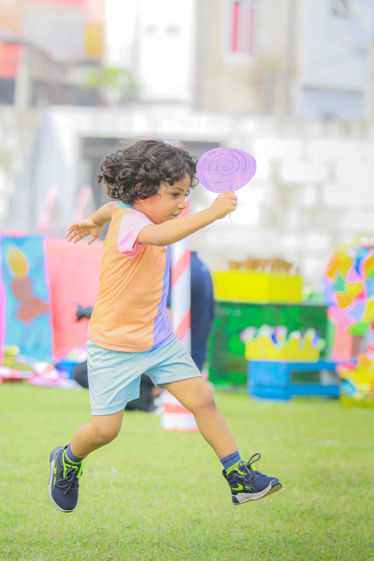 Energetic child running with paper fan at colorful outdoor event.