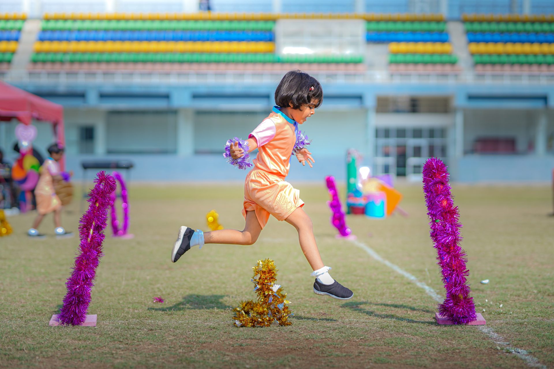 Child jumping over purple hurdle at colorful school sports day.