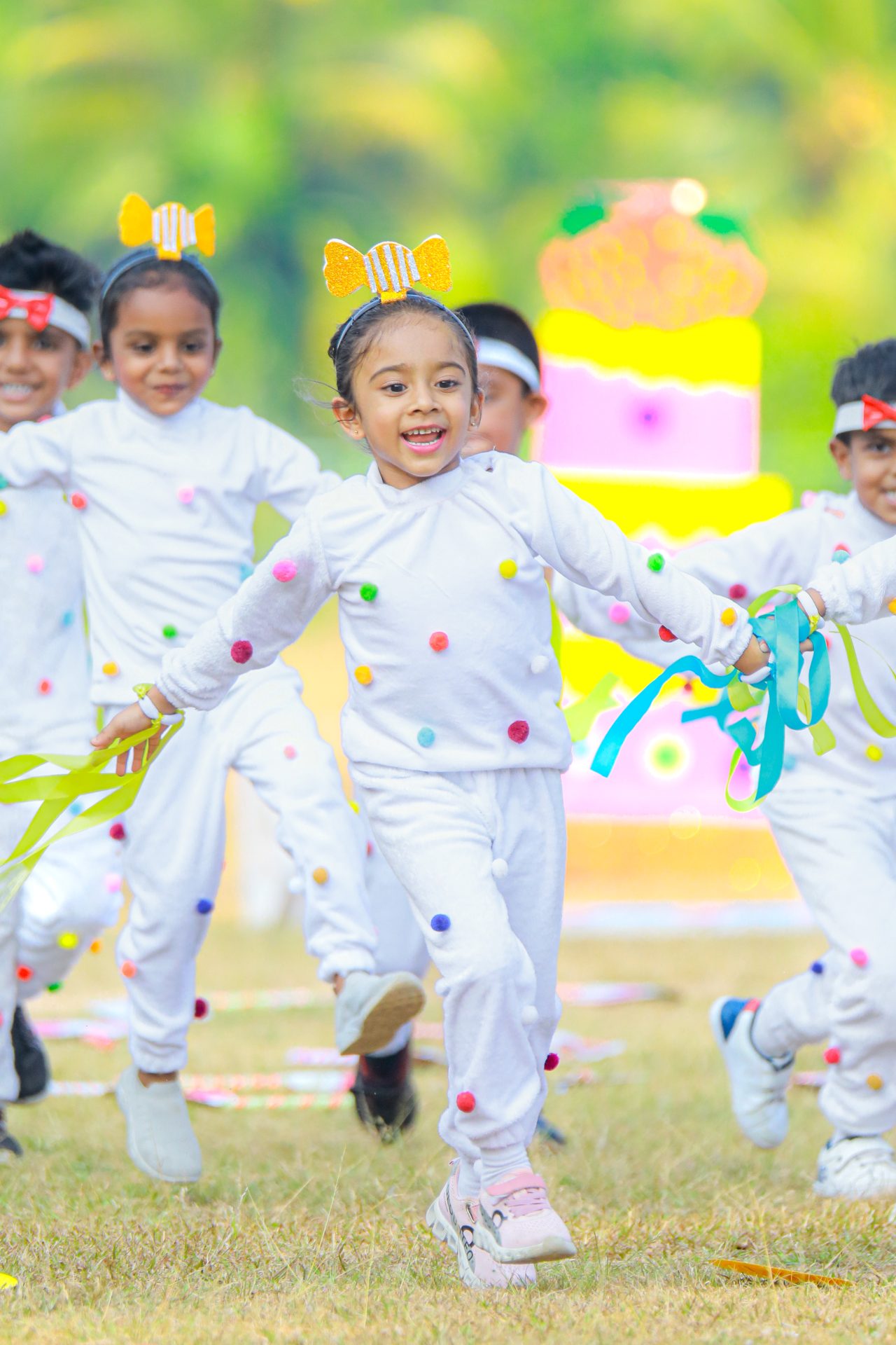 Children running outdoors in colorful polka dot outfits, waving streamers and smiling.