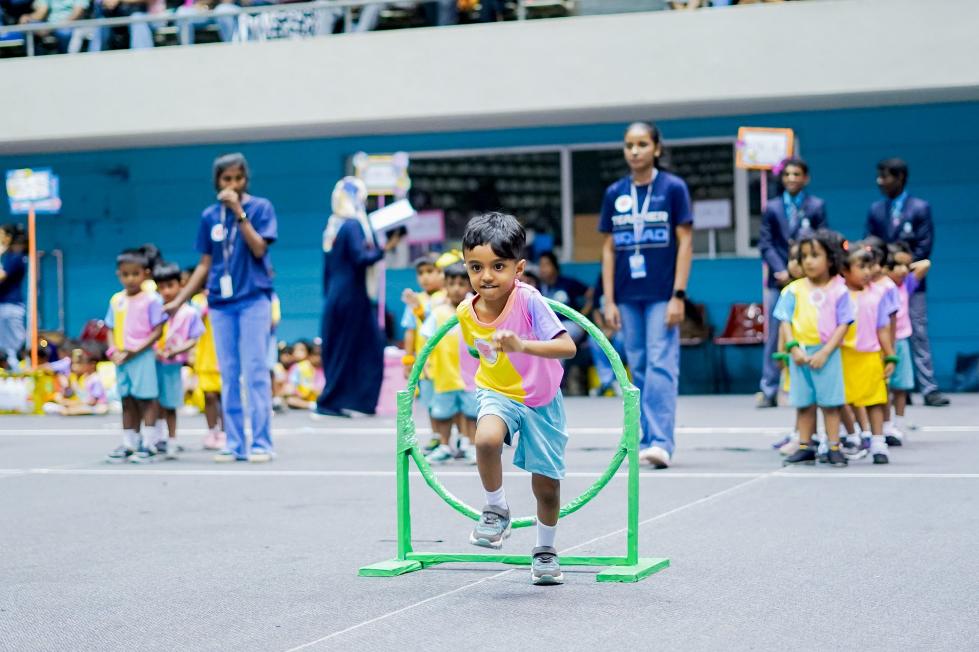 Boy running through hoop at childrens indoor sports event.