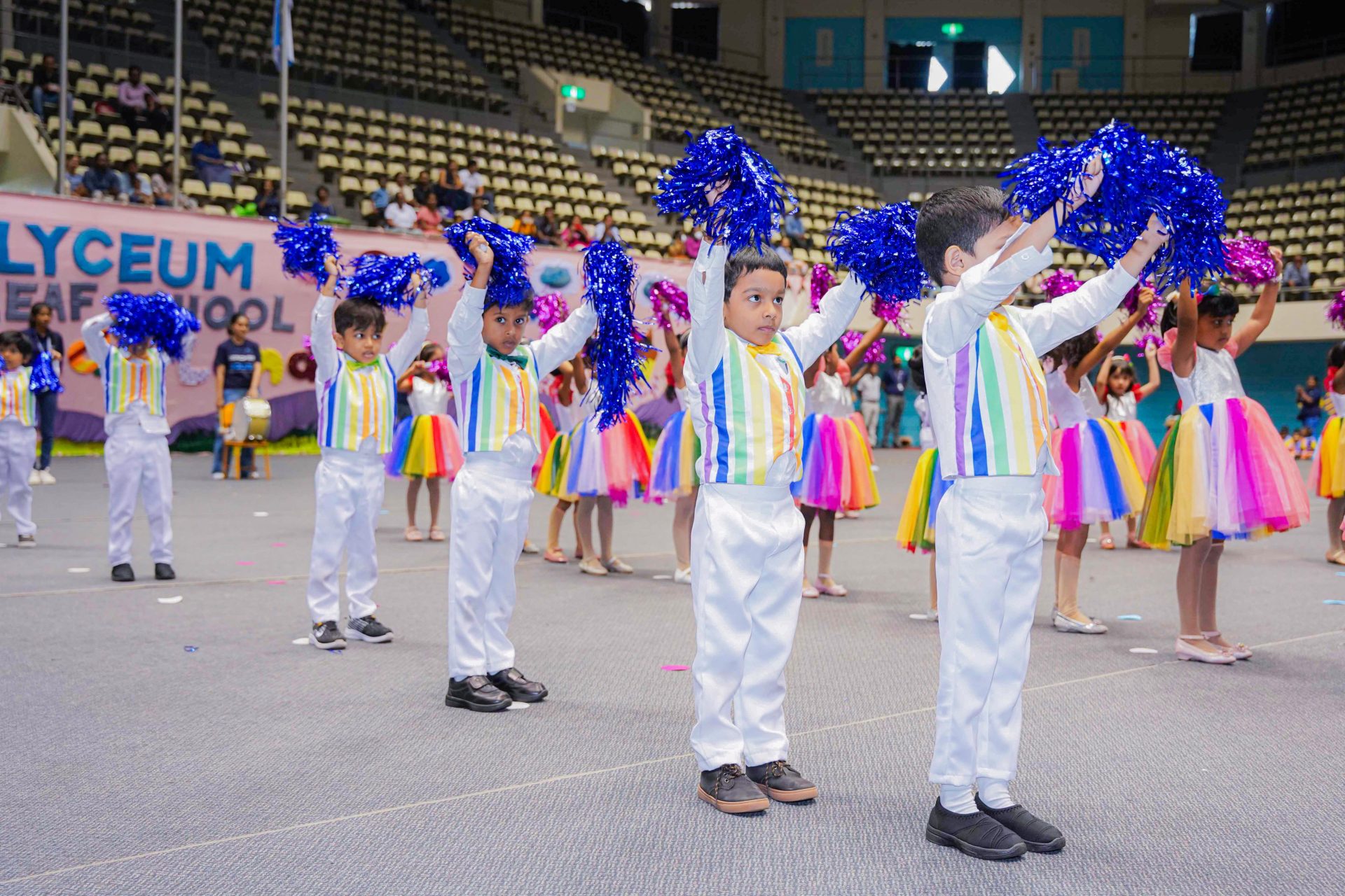 Children cheerleading in colorful costumes performing in a school gymnasium event.