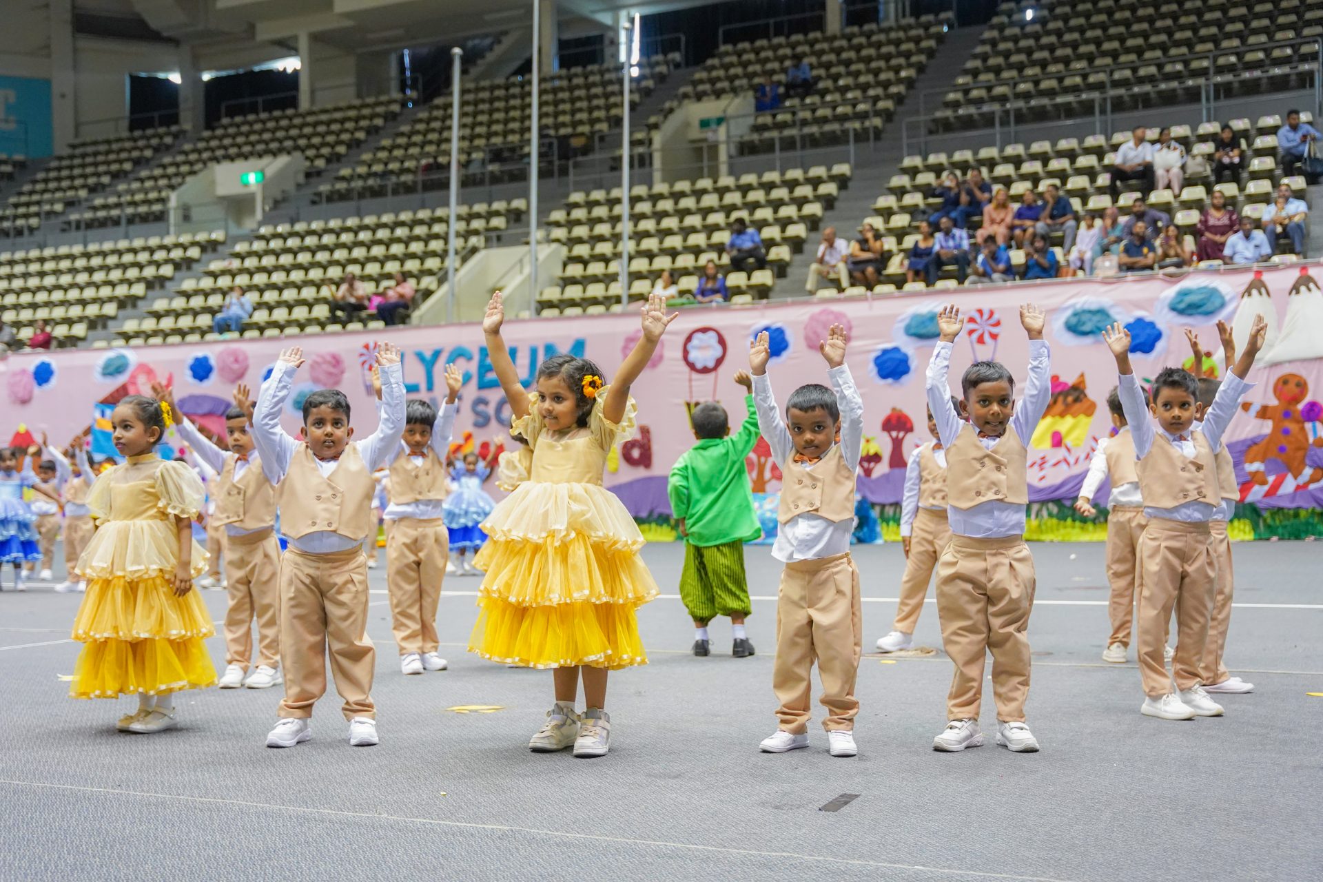 Childrens colorful dance recital in gymnasium with festive costumes and audience.