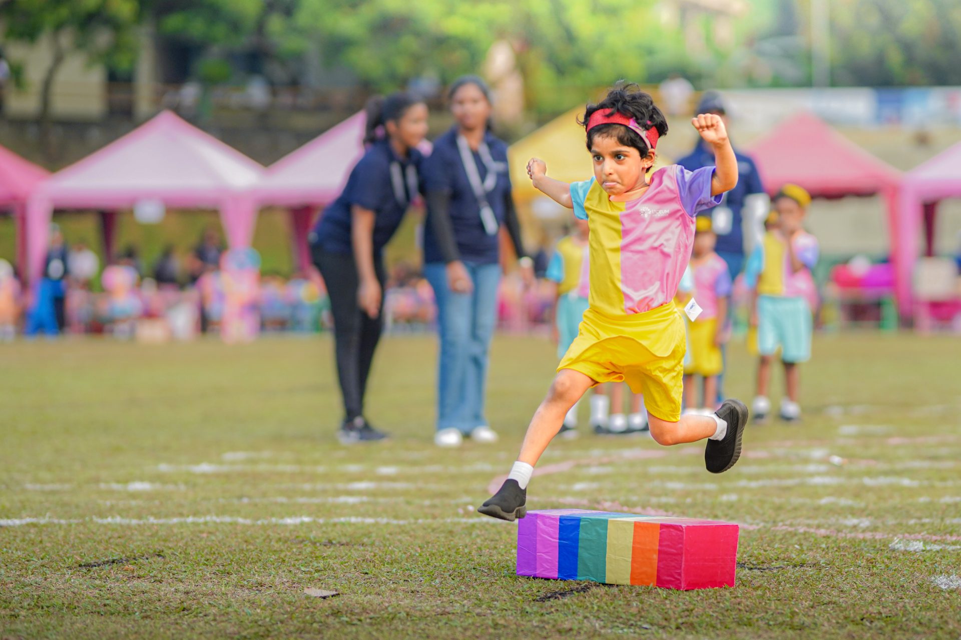 Child jumping over colorful blocks at outdoor sports day event.