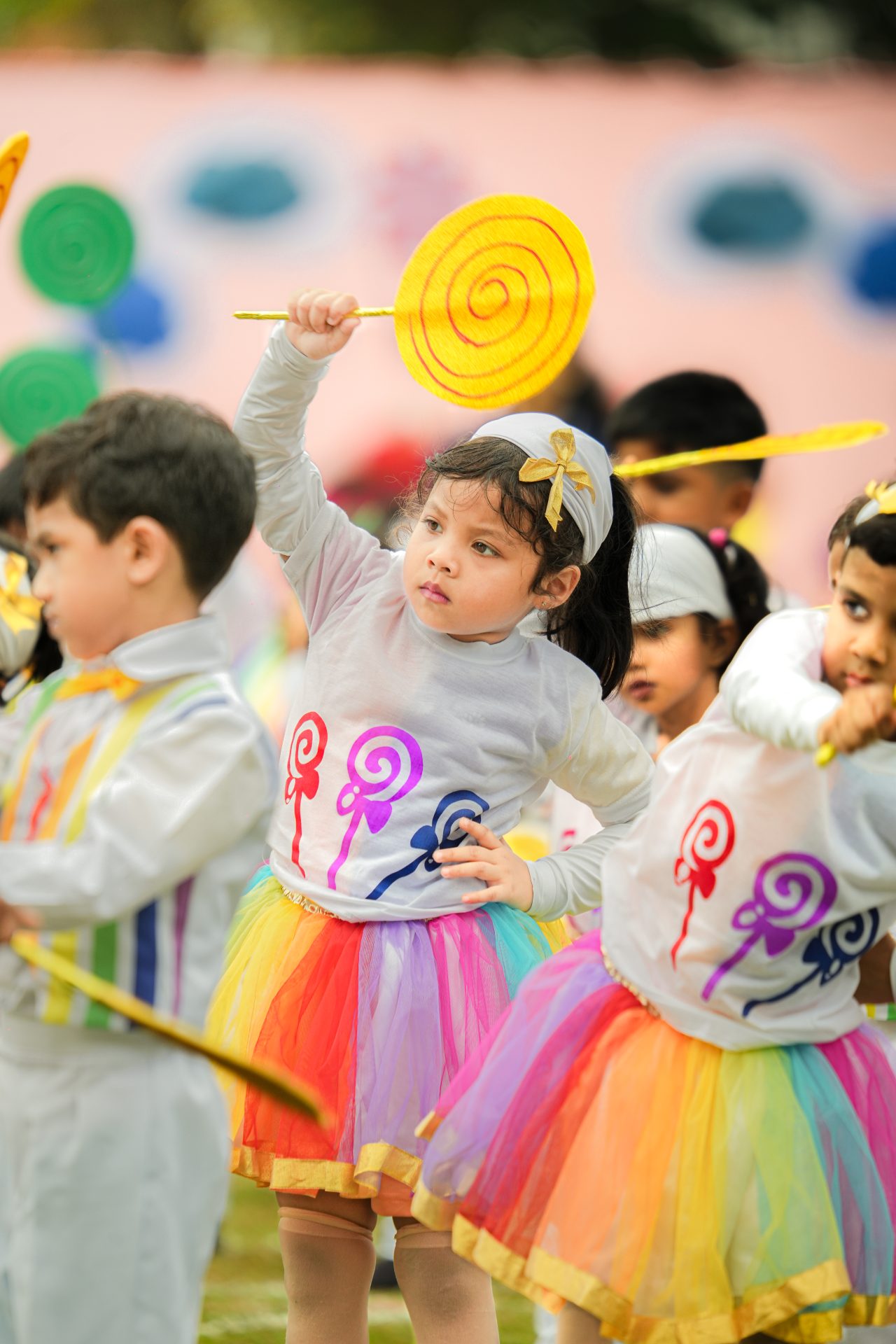 Children in colorful lollipop-themed costumes perform at a festive school event.