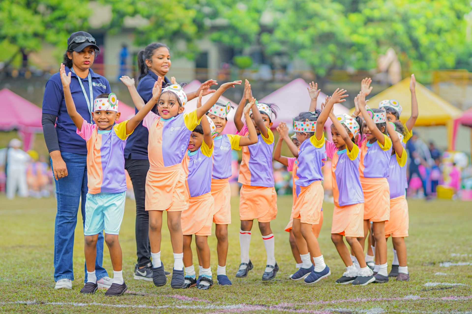 Children engaged in a lively sports day, guided by instructors on a grassy field with colorful tents.