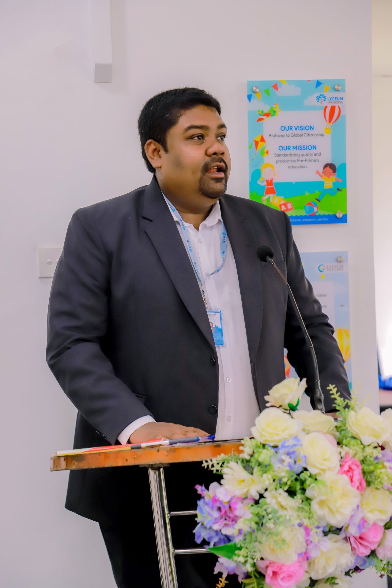 Man delivers speech at podium with flowers at educational conference.
