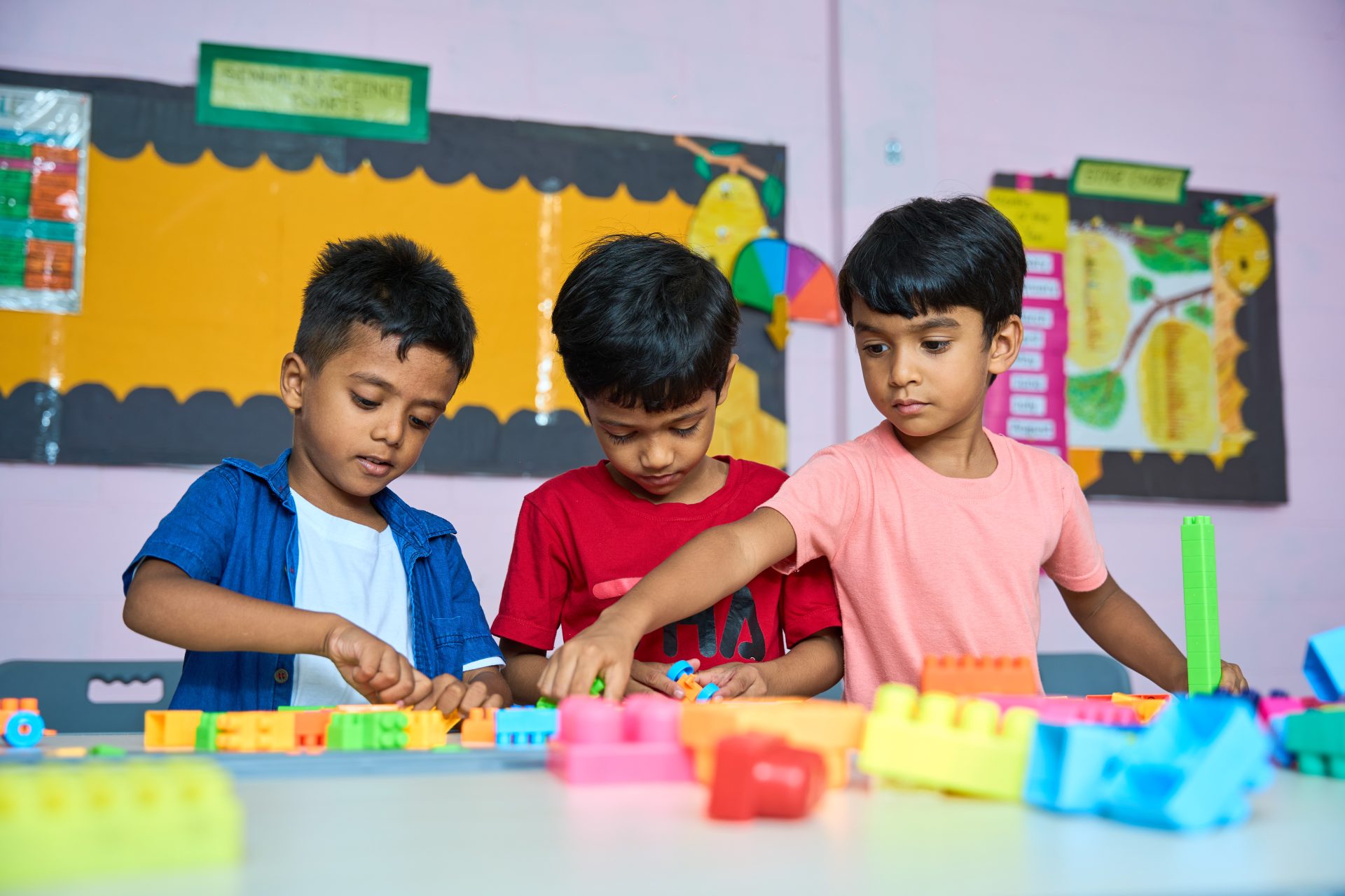 Three boys building with colorful blocks in a vibrant, educational classroom.