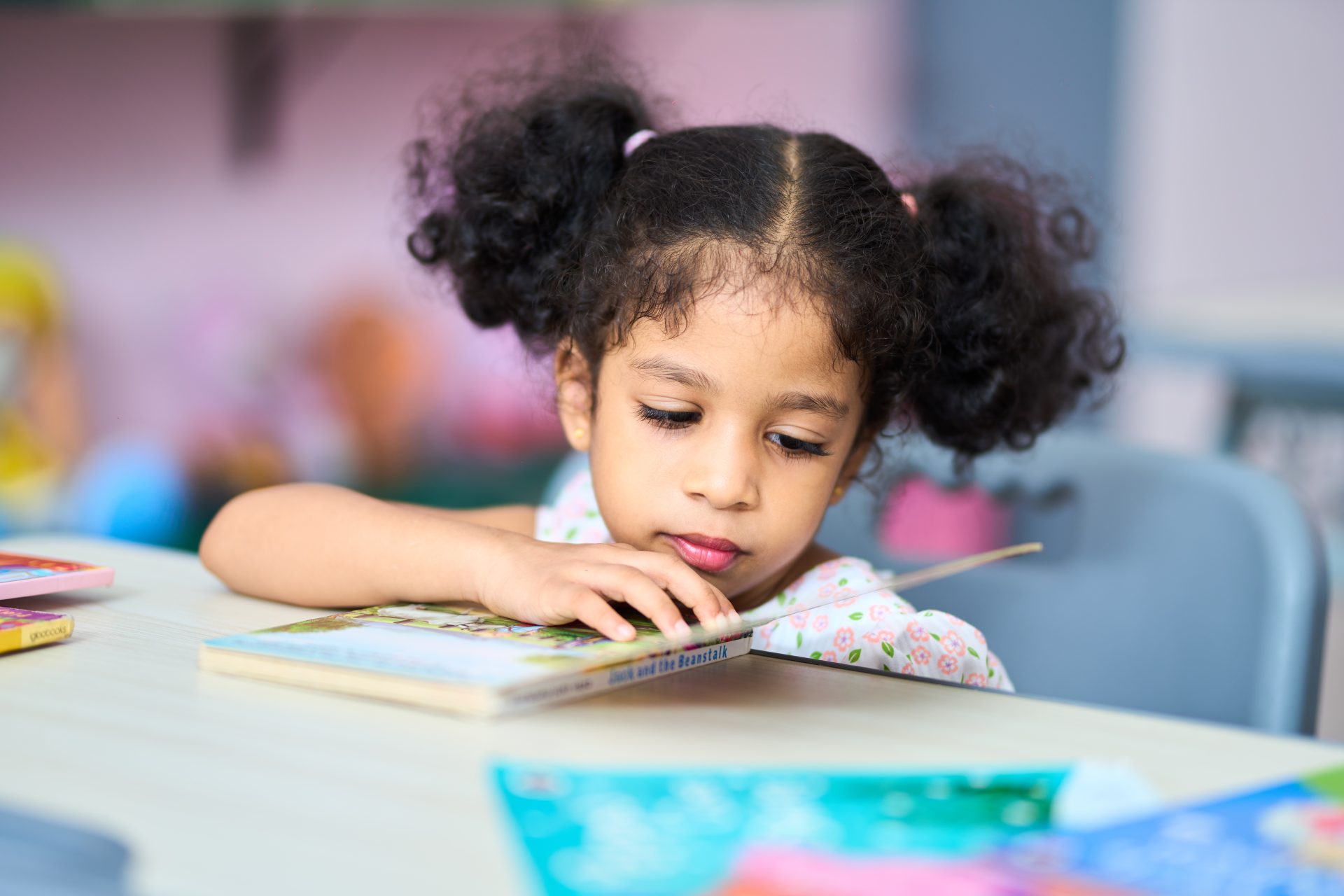 Preschool girl reading attentively in a colorful, child-friendly setting.