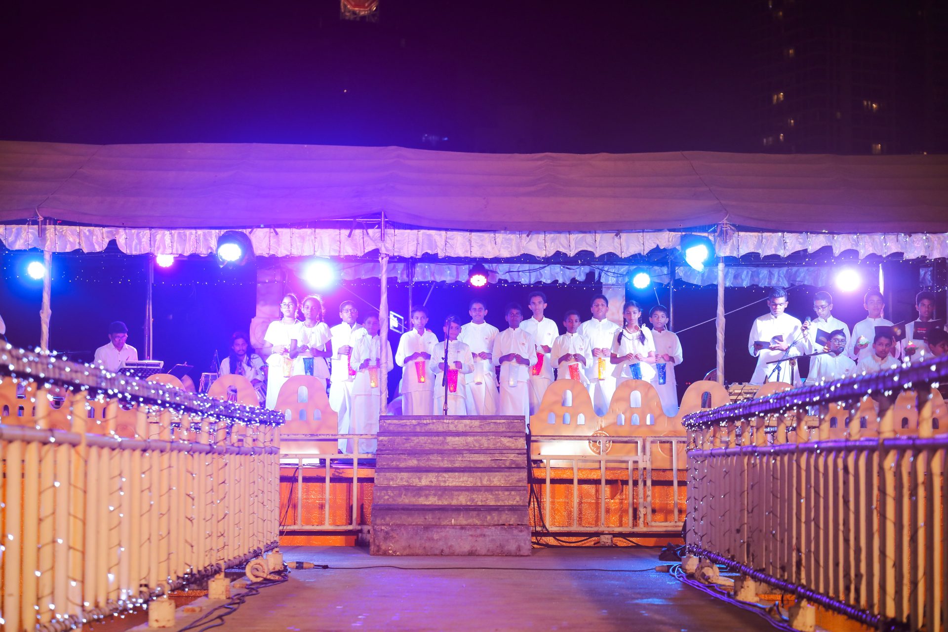 Nighttime choir performance on a brightly lit, decorated stage with young participants.