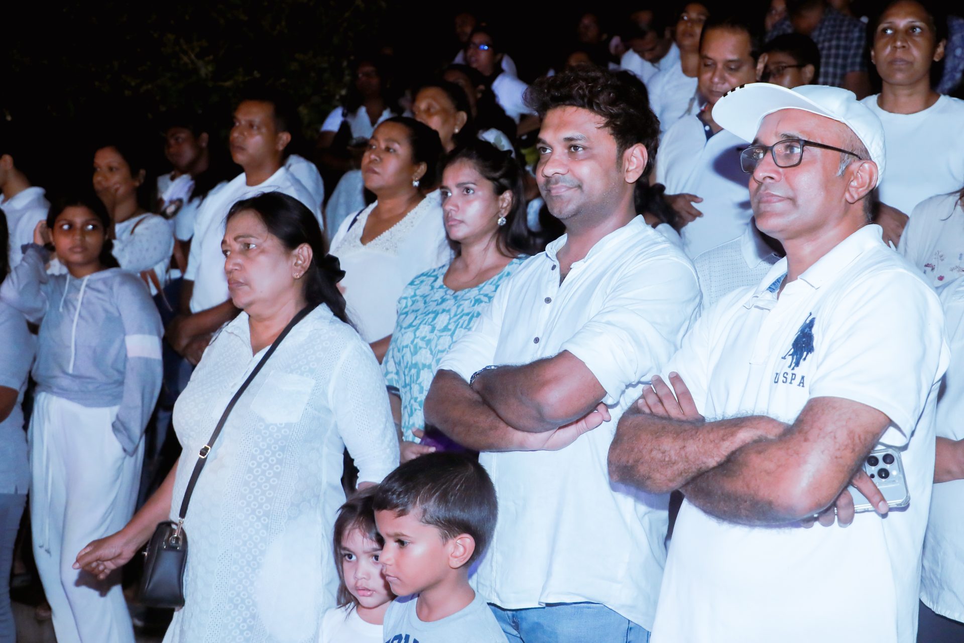 A diverse group at a night vigil, dressed in white, standing attentively.