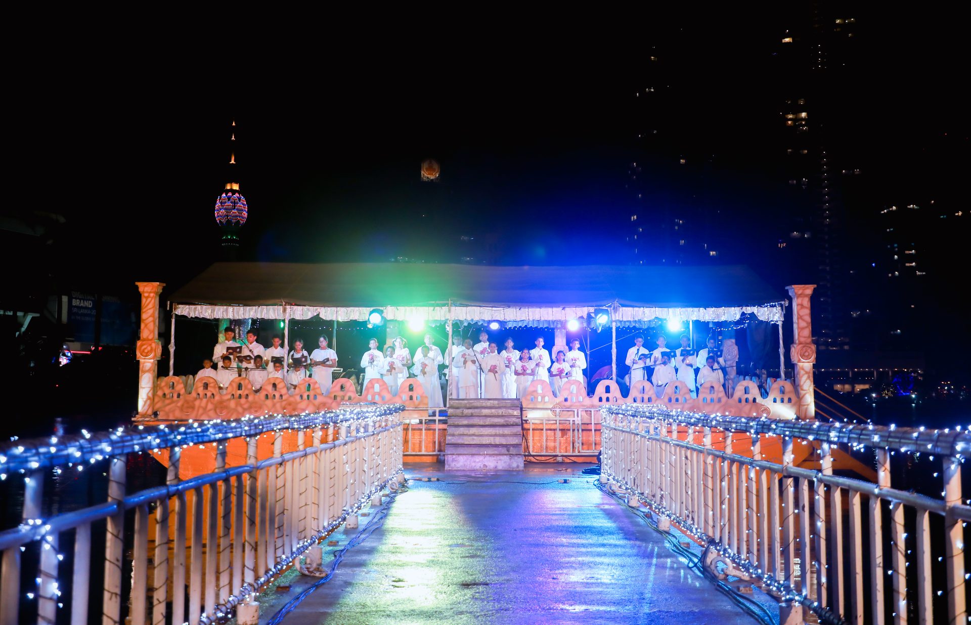 Nighttime urban performance on illuminated stage with decorative pathway and brightly lit tower.