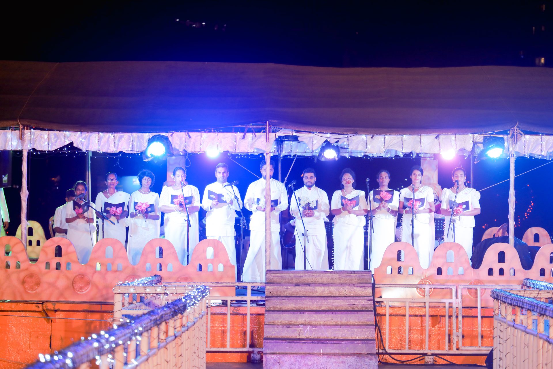 Performers in white on decorated stage with vibrant lighting, cultural celebration.