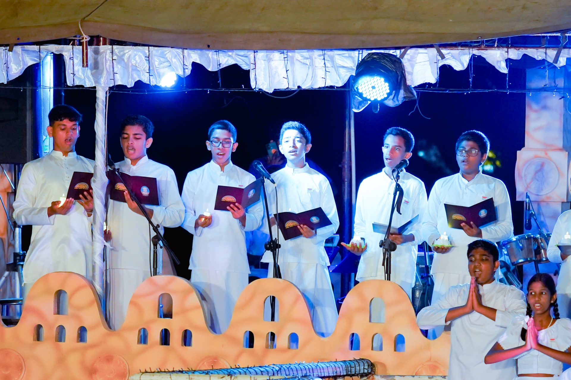 Young individuals in white attire performing with candles at a cultural event.