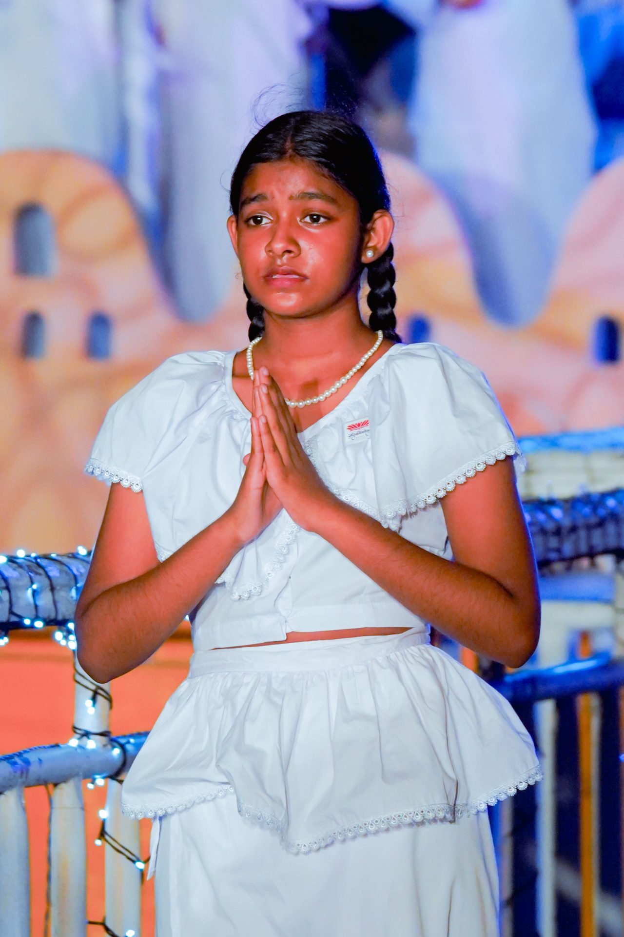 Young girl in white praying with braided hair and pearl necklace.