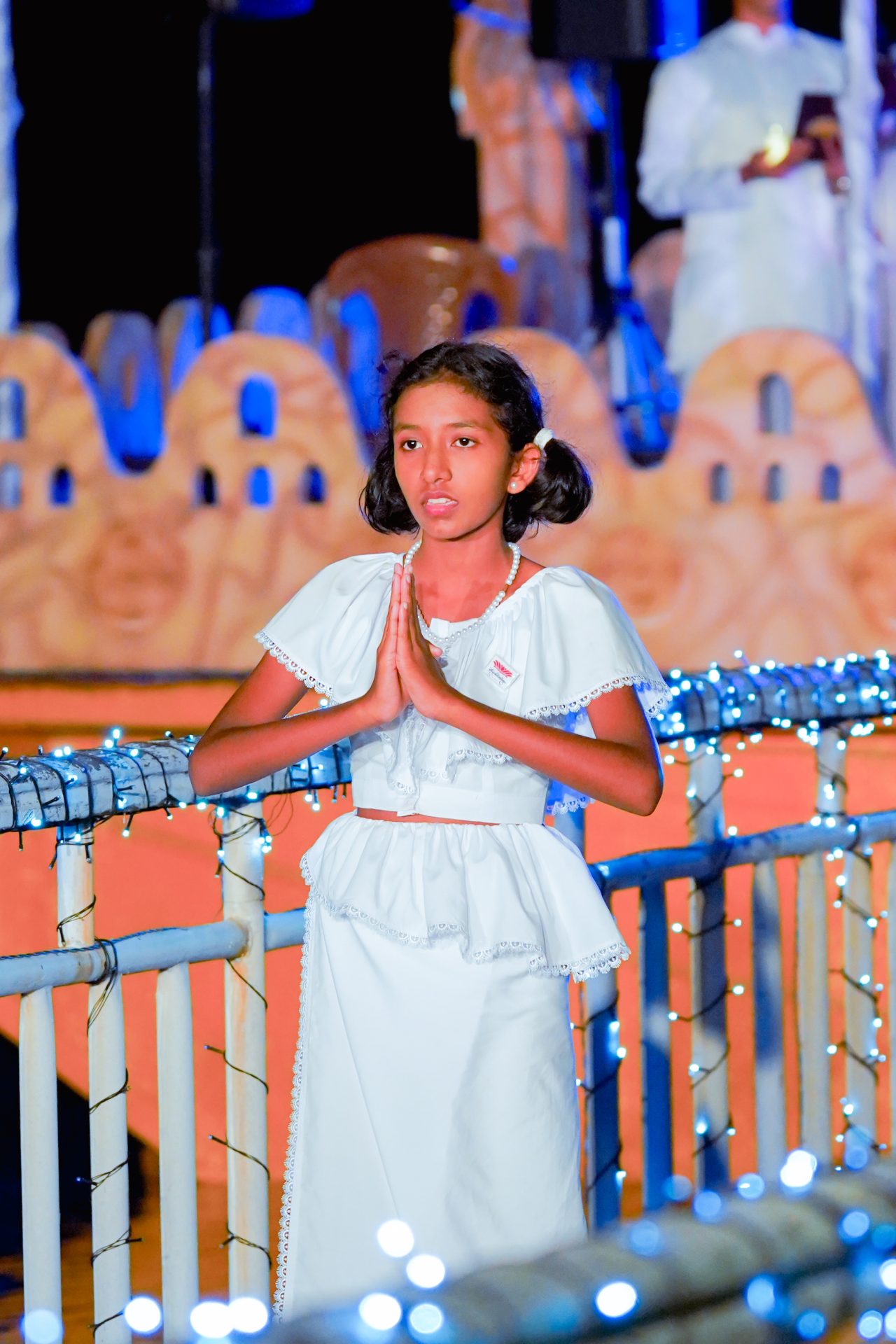Young girl in white praying at a festive ceremonial event.