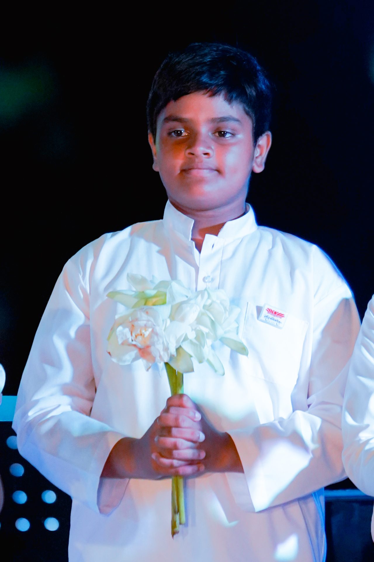 Young boy in traditional kurta holding bouquet of white flowers at a ceremony.