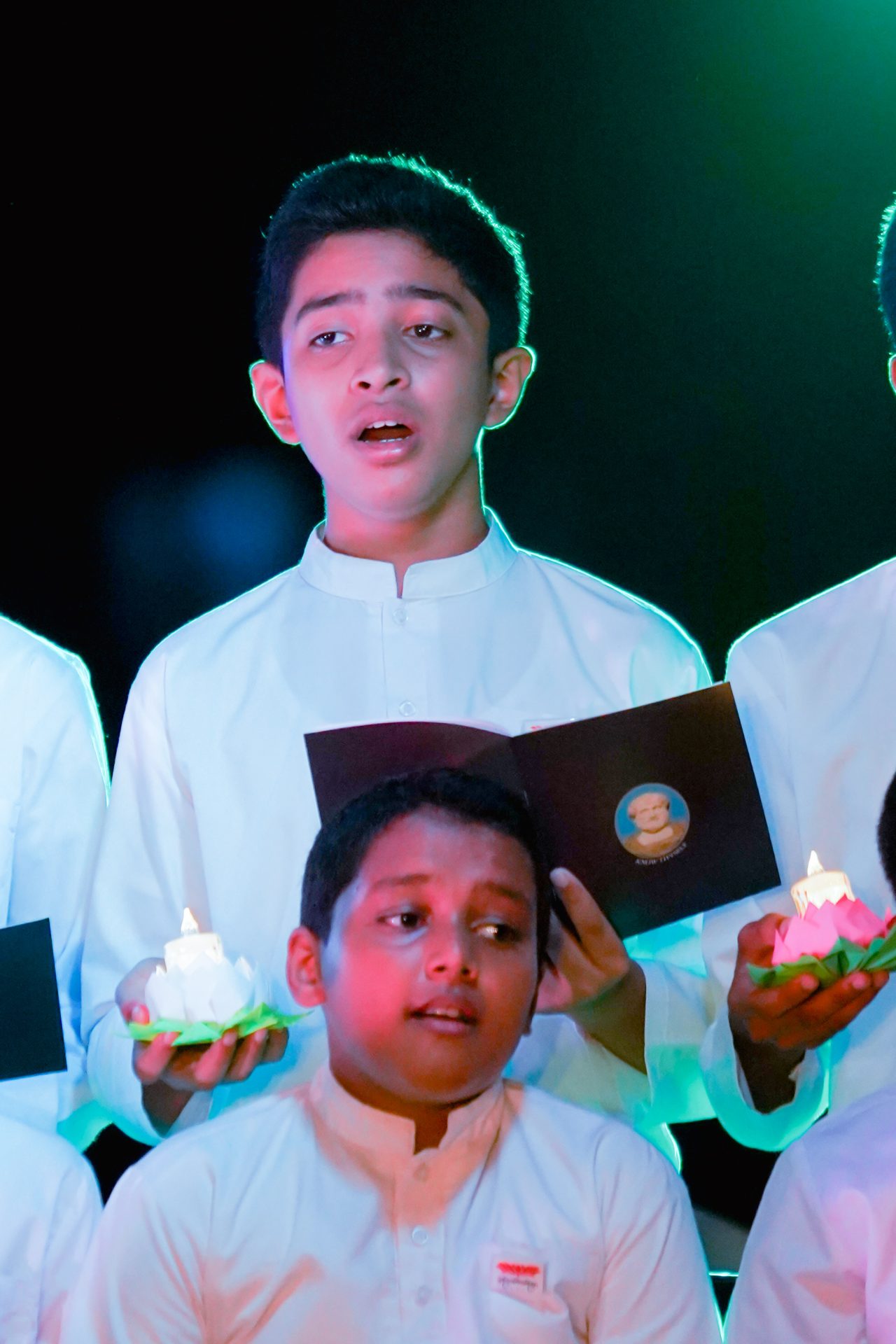 Boys in white attire holding candles during ceremonial event.