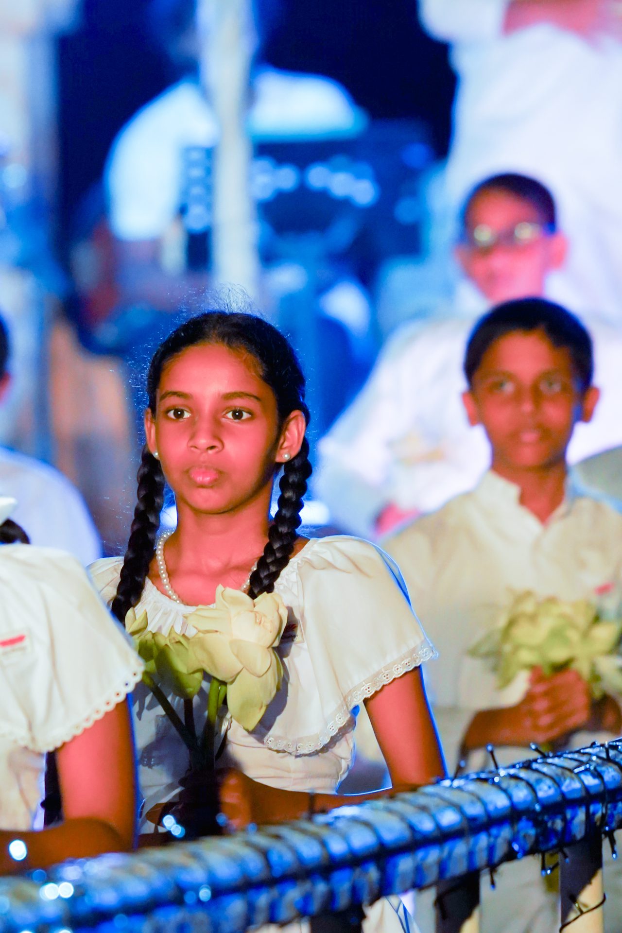 Children in white dresses holding flowers at a ceremony.